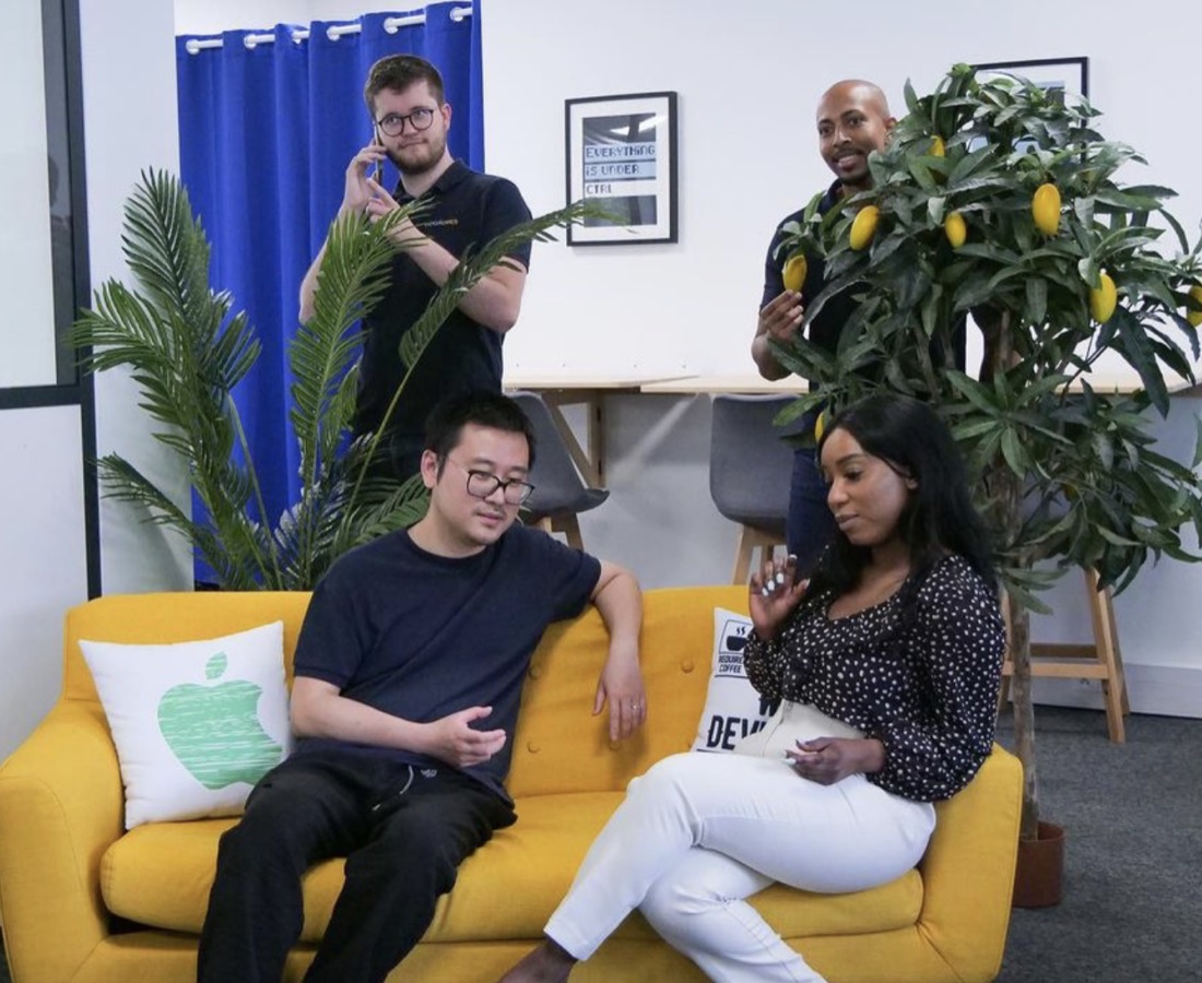 Deux collègues sur le canapé jaune des bureaux, un coussin « DEV » à côté d'eux